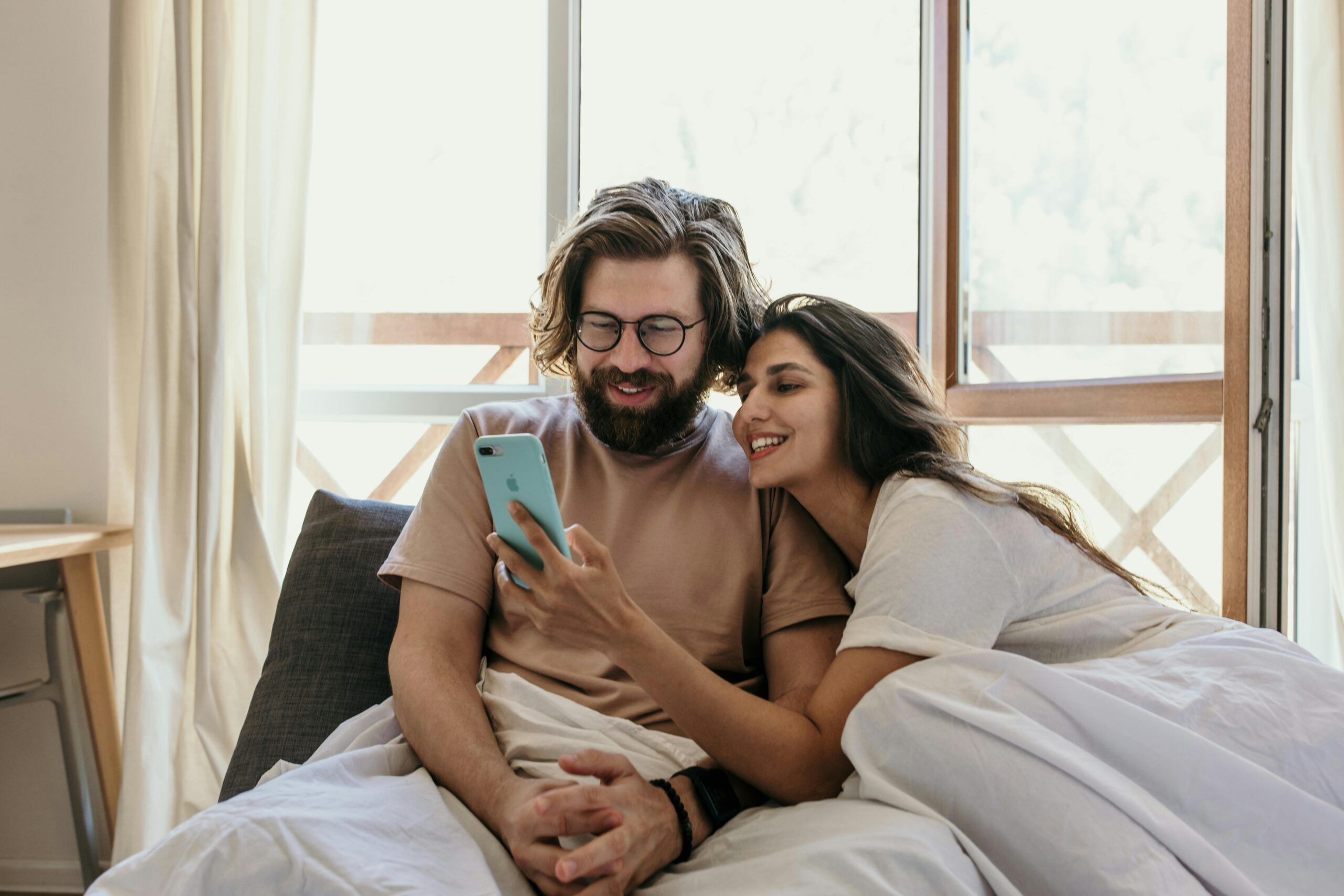 Couple looking at their phone and laughing in bed