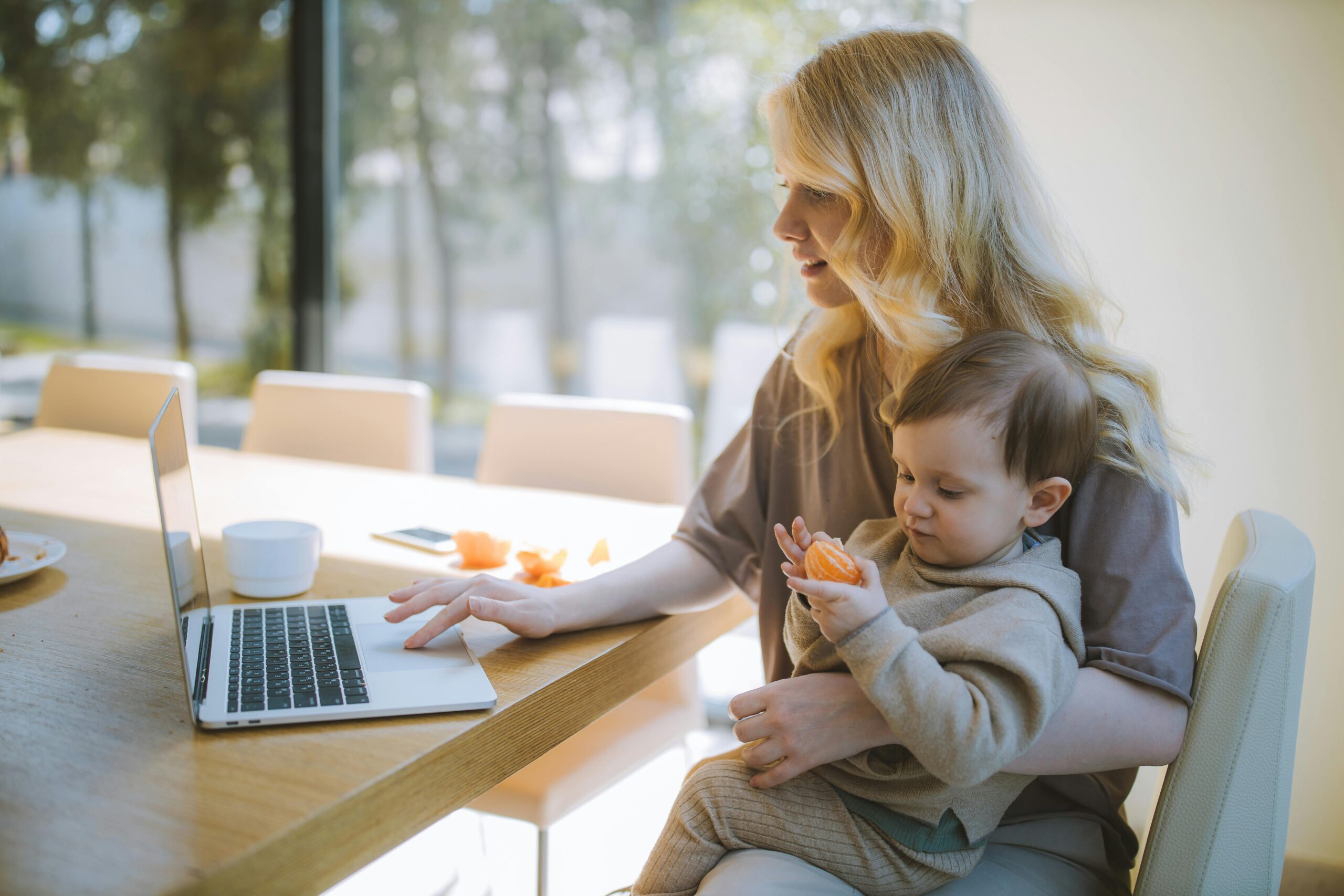 A working mom juggling work tasks on her laptop while holding a young child