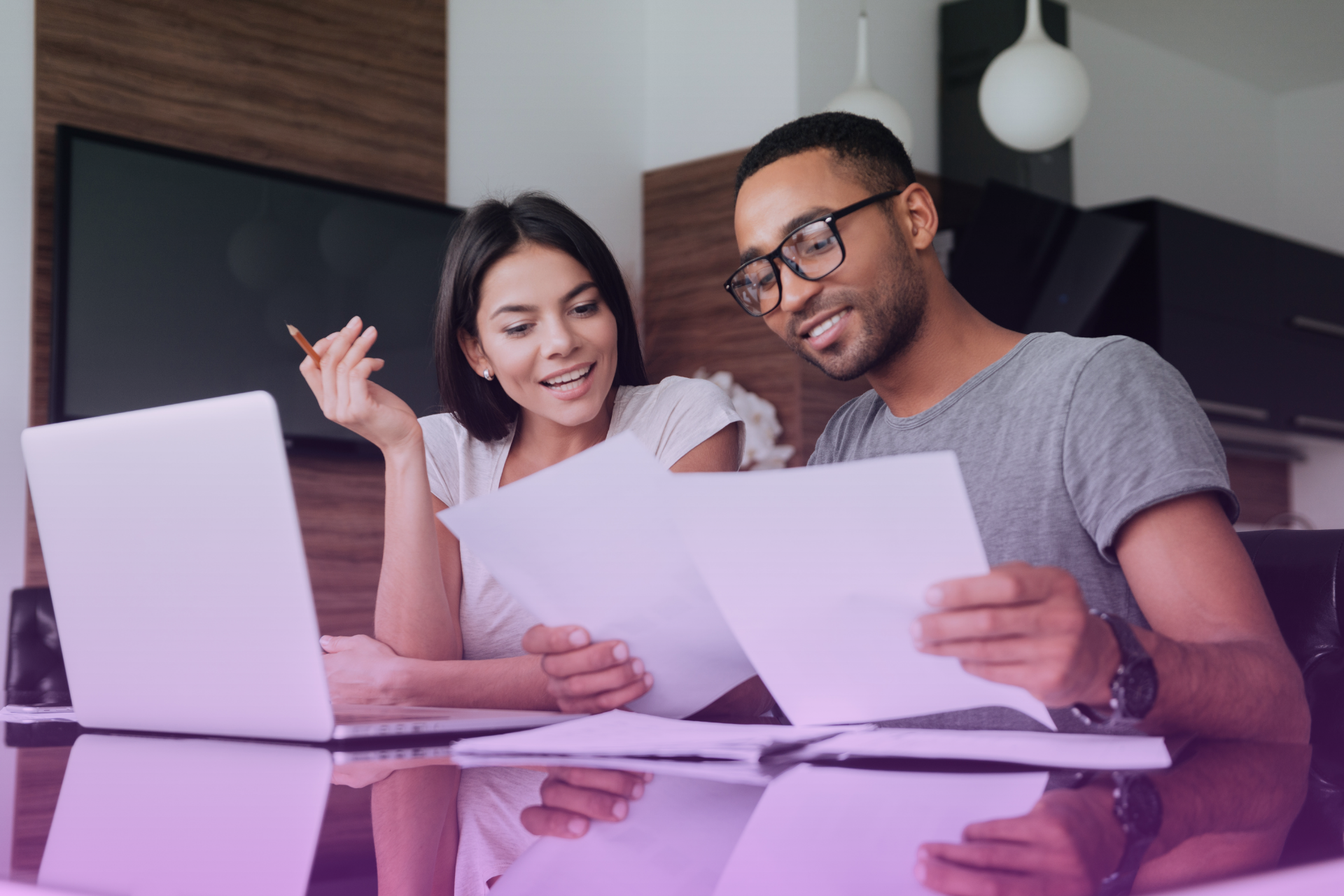 A happy couple talking about finances at a table, with paperwork spread out.