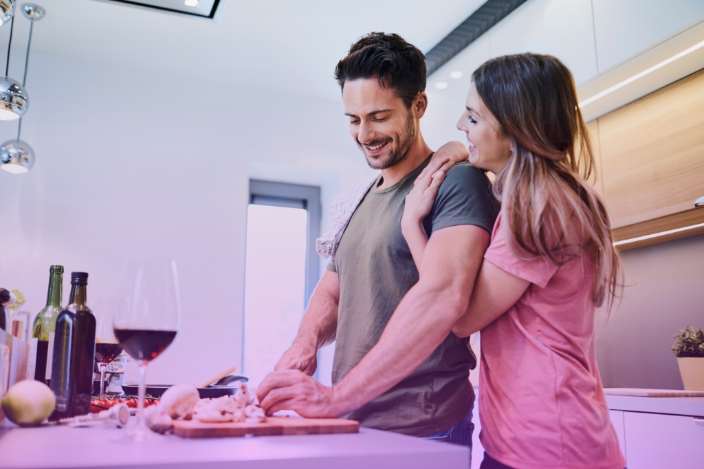 A diverse couple smiles and talks openly at a kitchen table, depicting open communication as a key to a healthy marriage.