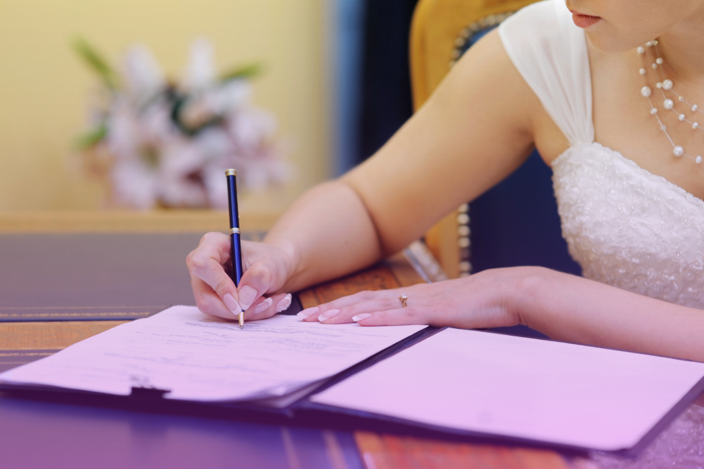 A close-up of a bride signing her marriage license, with a certified California marriage certificate prominently displayed.