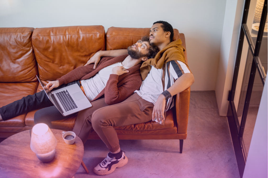 A married couple sits on a couch, talking and laughing with each other.