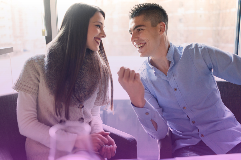 Smiling couple talking at a kitchen counter with a notebook and bills on the table.