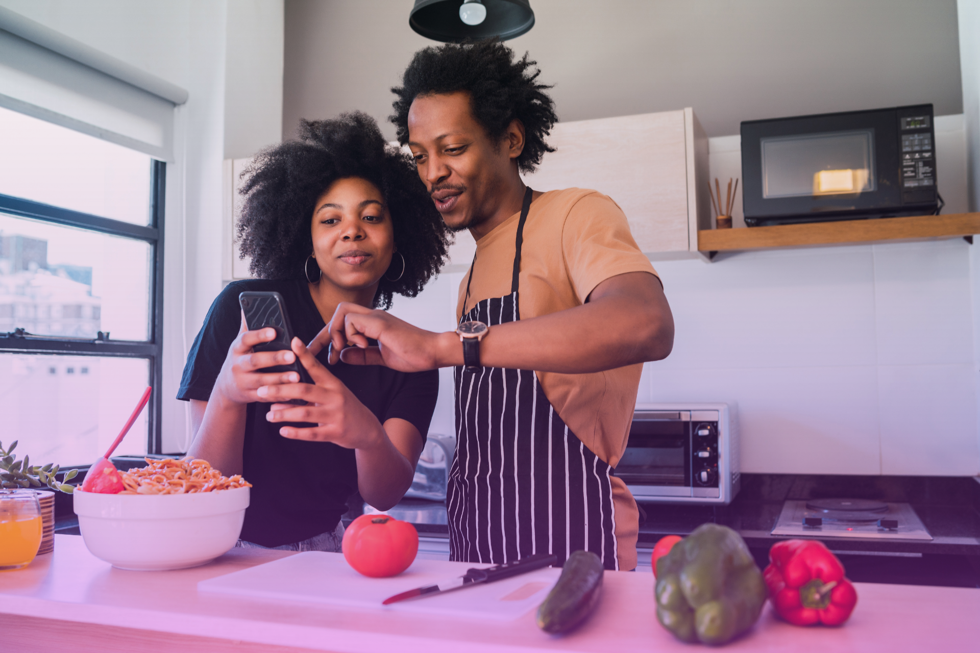 A young couple sits together, watching something funny on their cellphones and laughing.