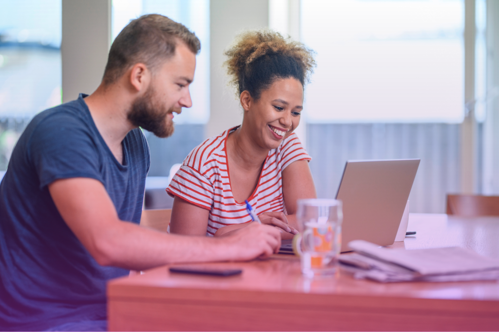 A diverse couple sitting together, looking at a budget worksheet and smiling.