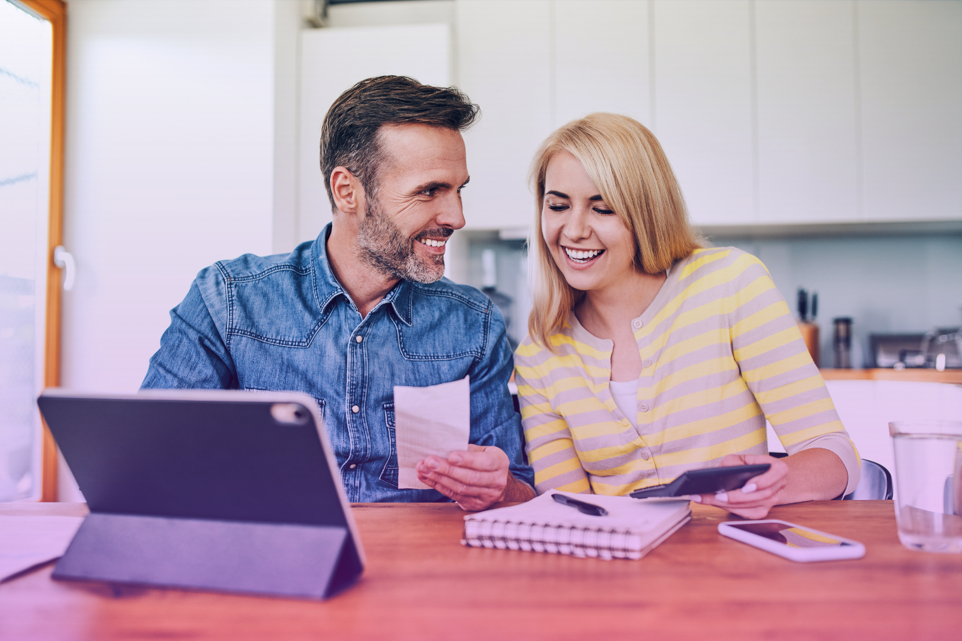 Happy couple reviewing finances together on a laptop, smiling and relaxed.