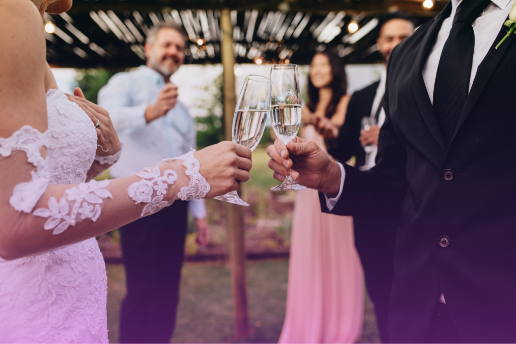 A newly married couple smiles and clinks champagne glasses in celebration.