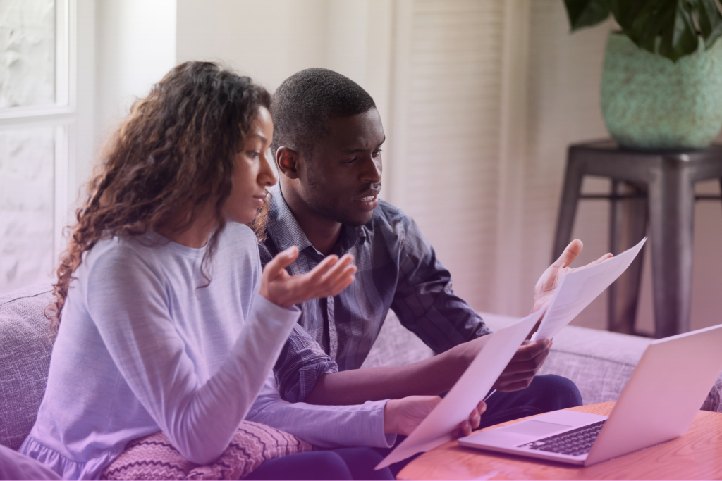  couple sits frustrated at a table looking at bills and bank statements.
