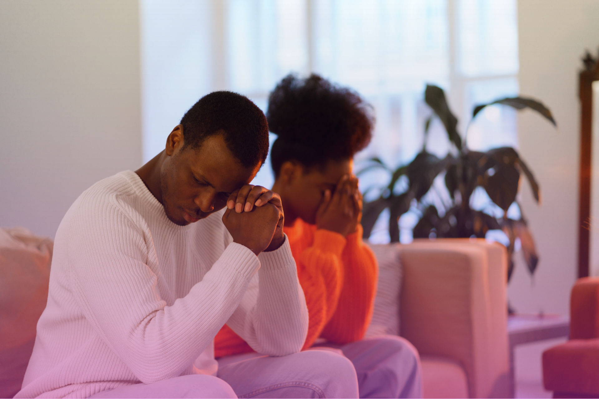 A sad couple sitting on a couch, turned away from each other.