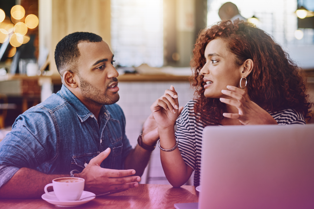 Married couple sitting at a table, facing each other and talking seriously.