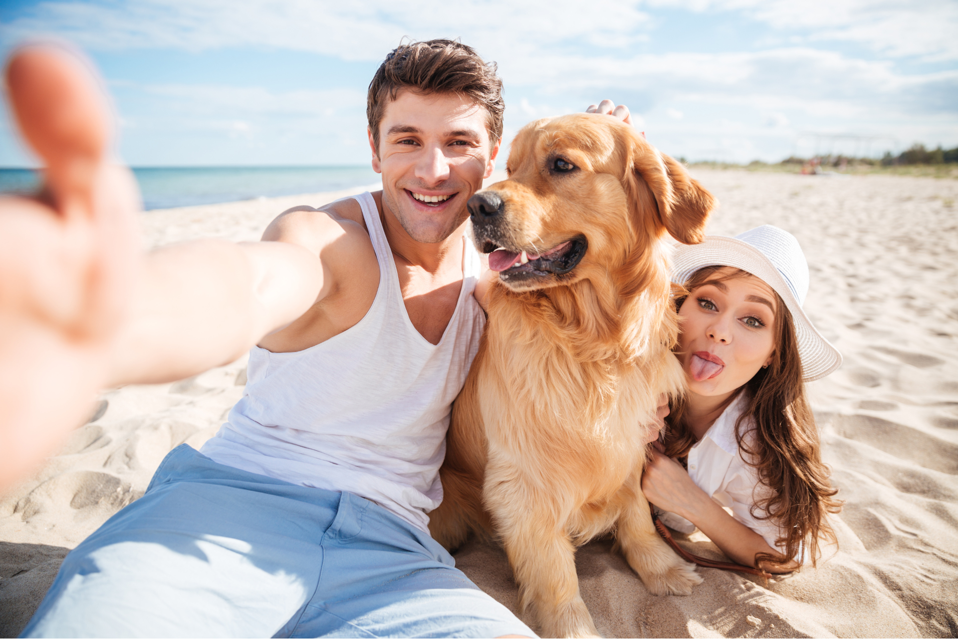 Man taking a selfie with his wife and their dog on a sunny beach.