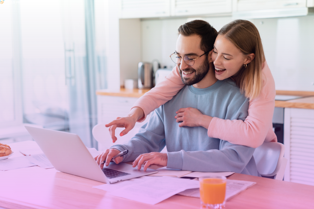 A happy couple sitting on a couch, looking at a laptop and researching prenuptial agreements.