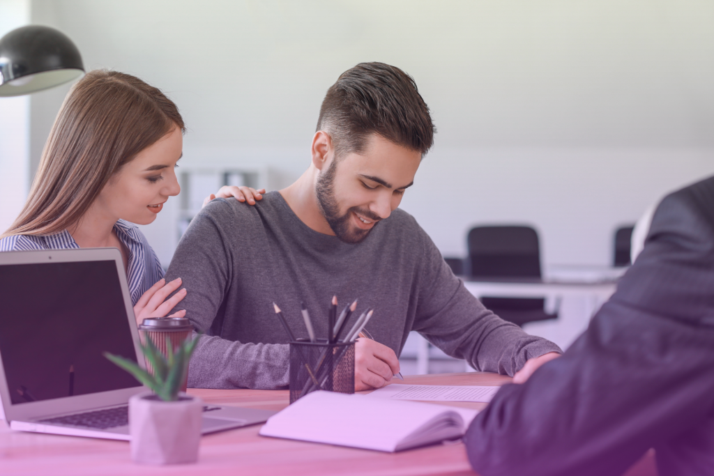 A happy Oklahoma couple sitting at a table signing a document, with a wedding band in the background.