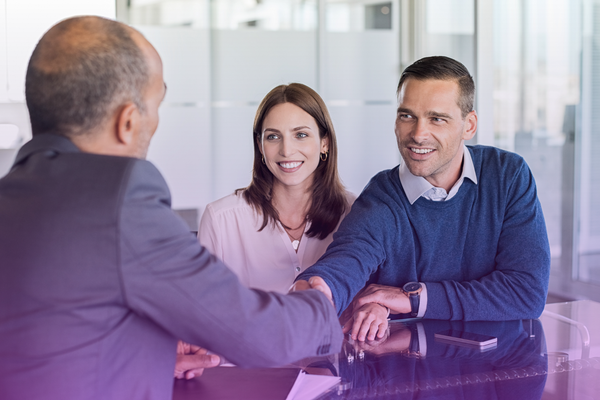 A smiling couple sitting at a table reviewing a document together with an attorney symbolizing open communication about finances.