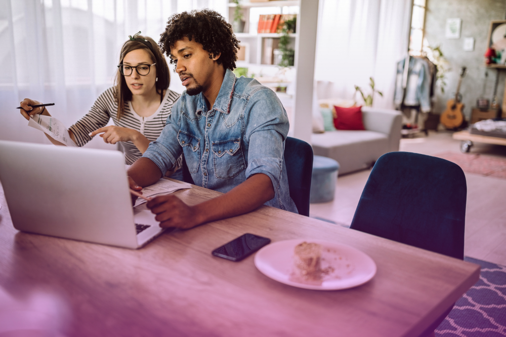 A Latino and an American partner sit side by side, focused on a laptop screen as they review important details, showcasing teamwork and cultural diversity.