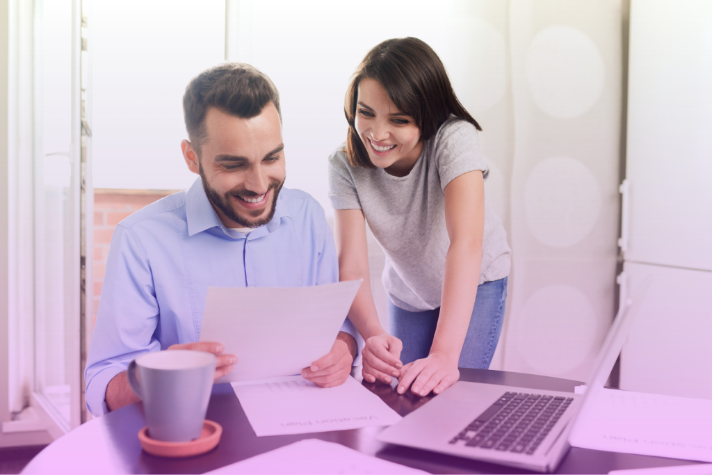 A couple sitting at a table, focused on reviewing a document and a laptop, symbolizing decision-making and planning for prenuptial and postnuptial agreements.