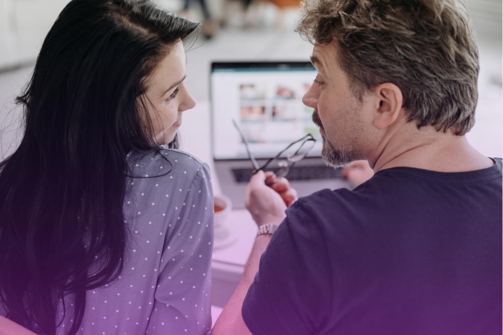 A happy couple talking at a table with a document titled "Postnuptial Agreement" and a document titled "Inheritance" visible, symbolizing a postnup discussion about inheritance.