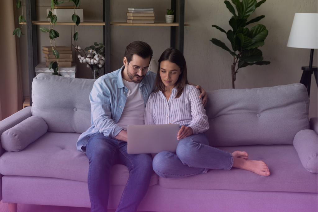 A happy couple smiling and looking at a laptop screen, possibly discussing a postnuptial agreement and feeling relieved after addressing initial resistance.