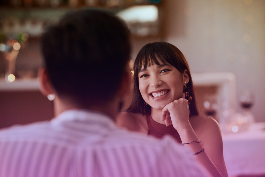 Two people on a first date sitting on a park bench, engaged in a deep conversation with smiles on their faces.