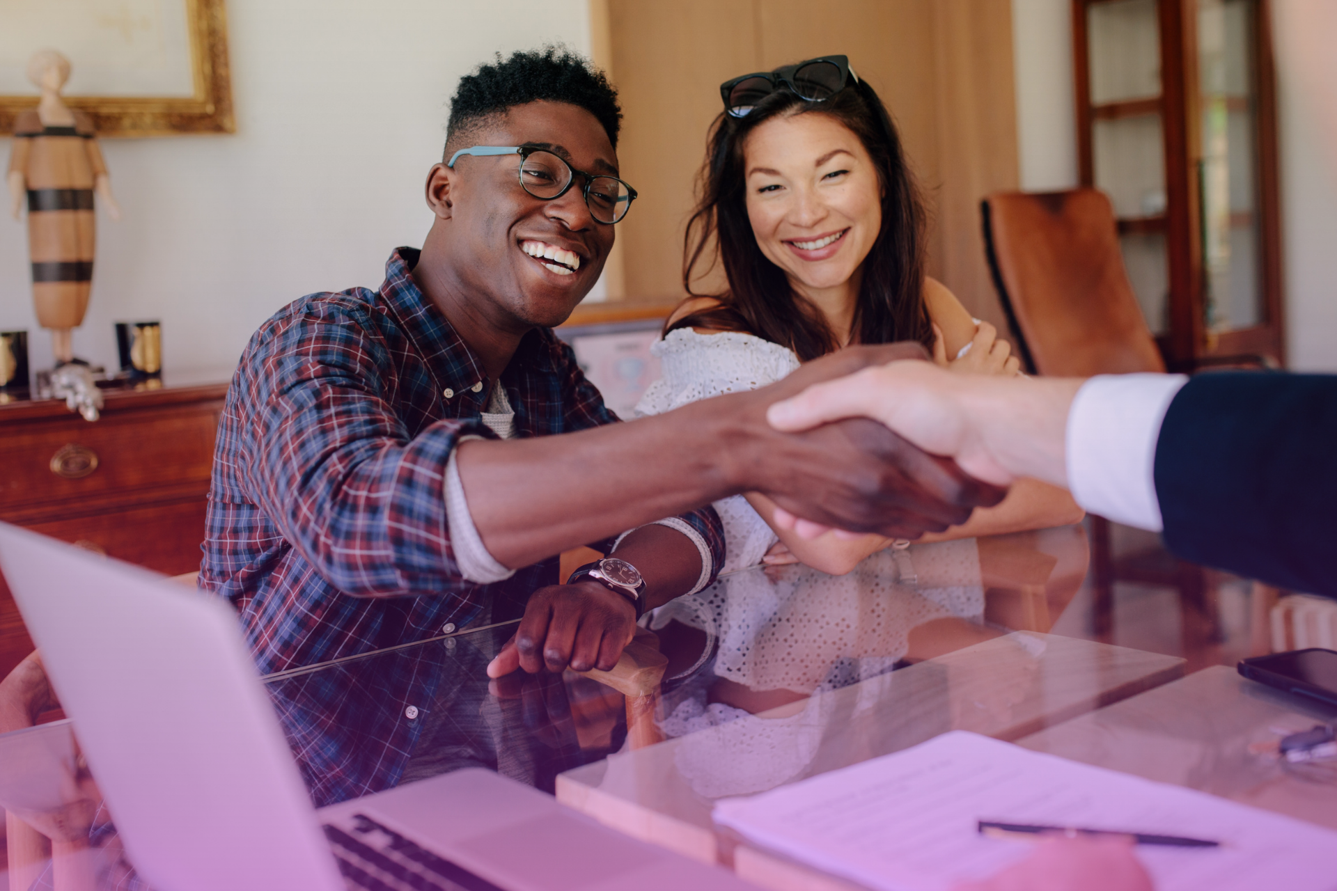 A happy couple smiling and shaking hands with a lawyer, signifying a successful postnuptial agreement process.