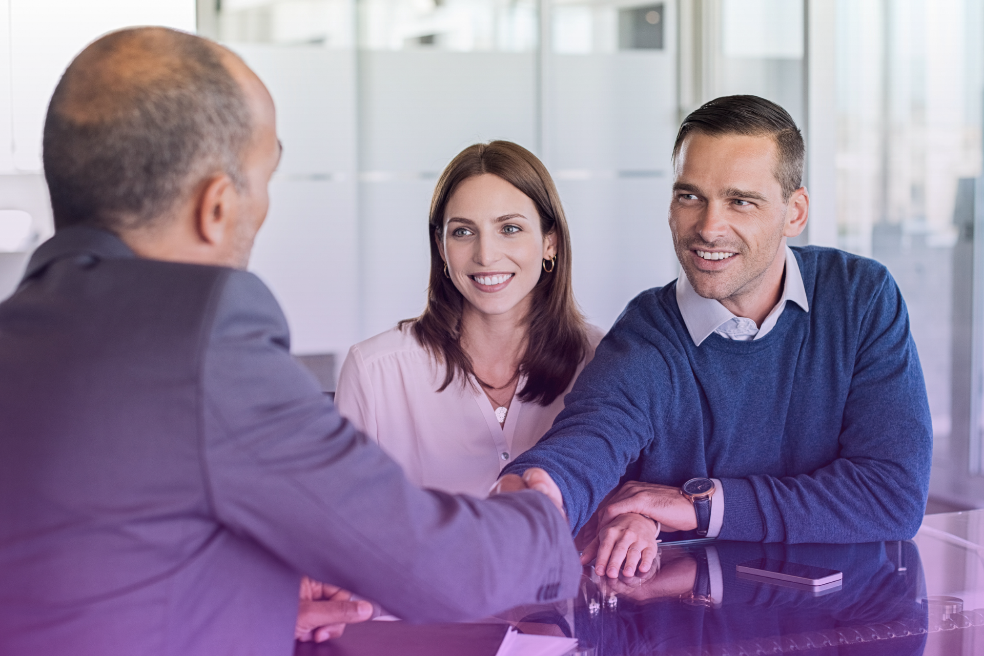 A couple shakes hands with a lawyer in a modern office setting, establishing a trusting relationship.