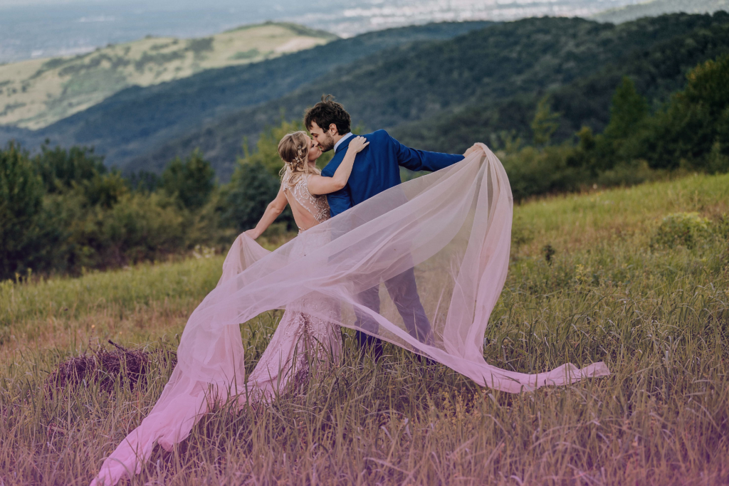 Happy couple celebrating their wedding day on a mountain, smiling and embracing with scenic views in the background.