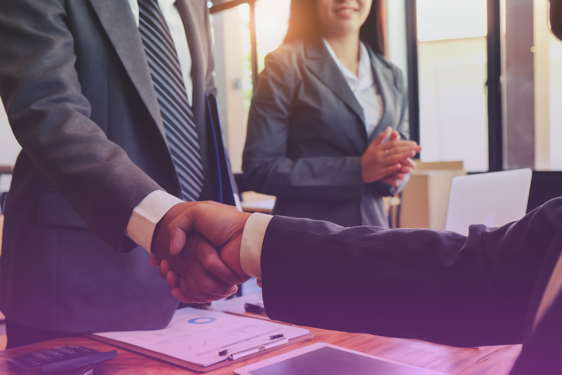 Two people shaking hands across a table with legal papers, symbolizing a mutually agreed-upon and properly executed agreement.
