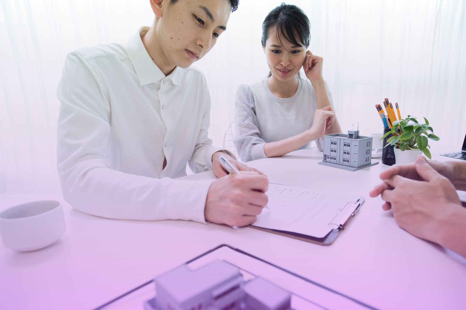 A couple signs a prenuptial agreement at a table, symbolizing the legal protection a prenup provides.