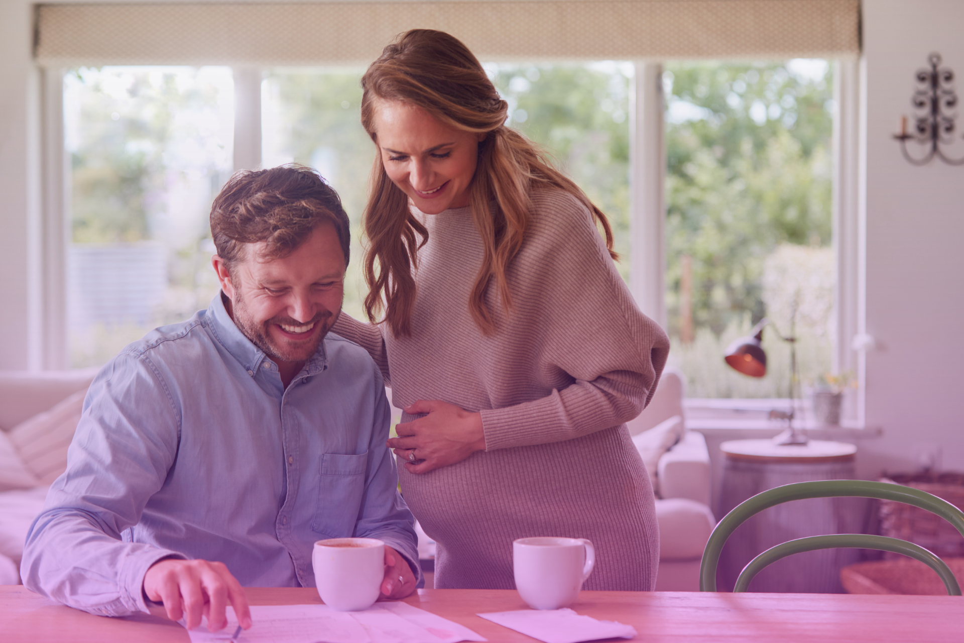A smiling couple sitting together and reviewing a checklist on a tablet, symbolizing a joint effort in planning for their future.