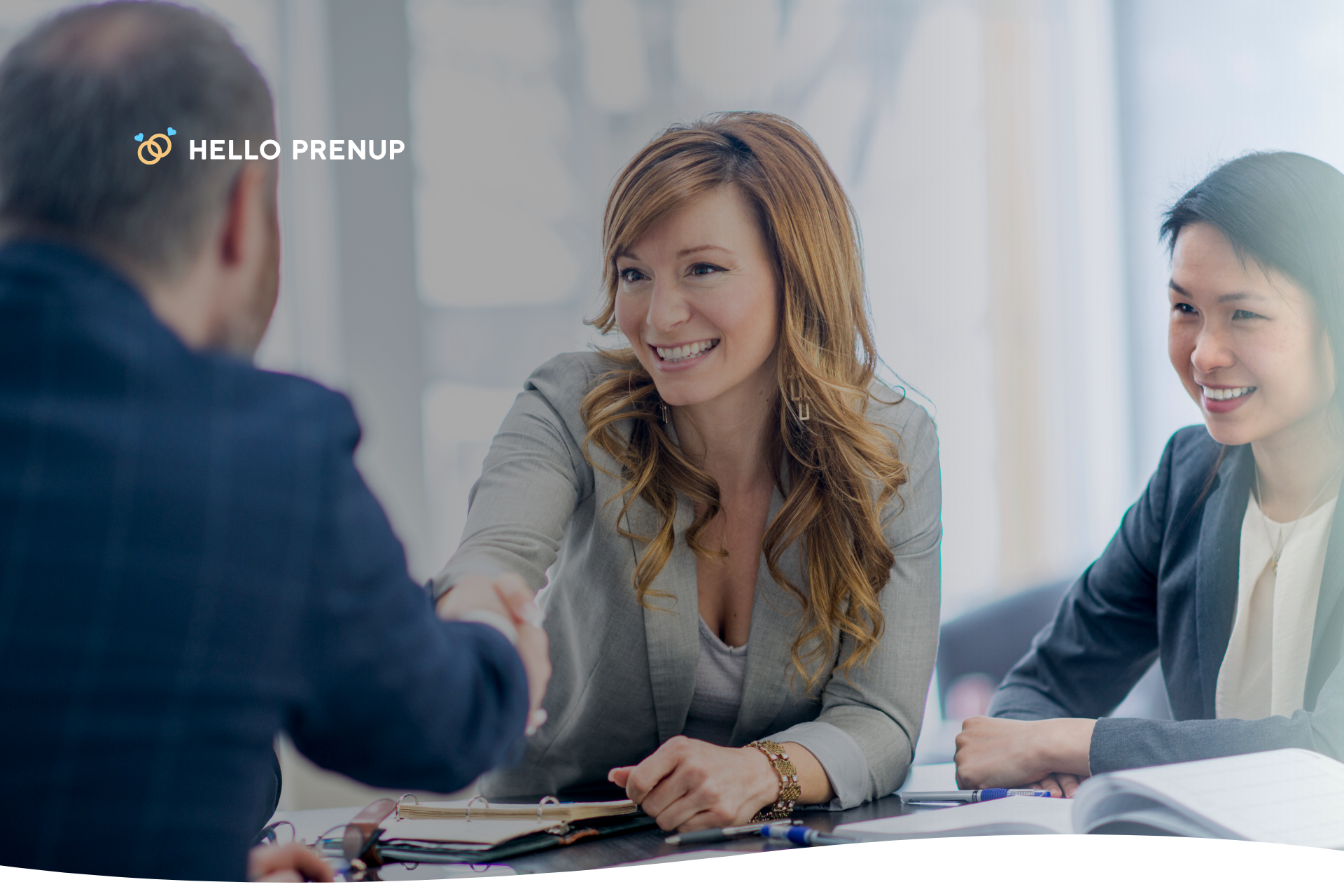 A couple sits at a table with an attorney, smiling and shaking hands over a document A couple seated at a table with an attorney, smiling and shaking hands, representing the retention of independent legal counsel for a Hawaii prenup.