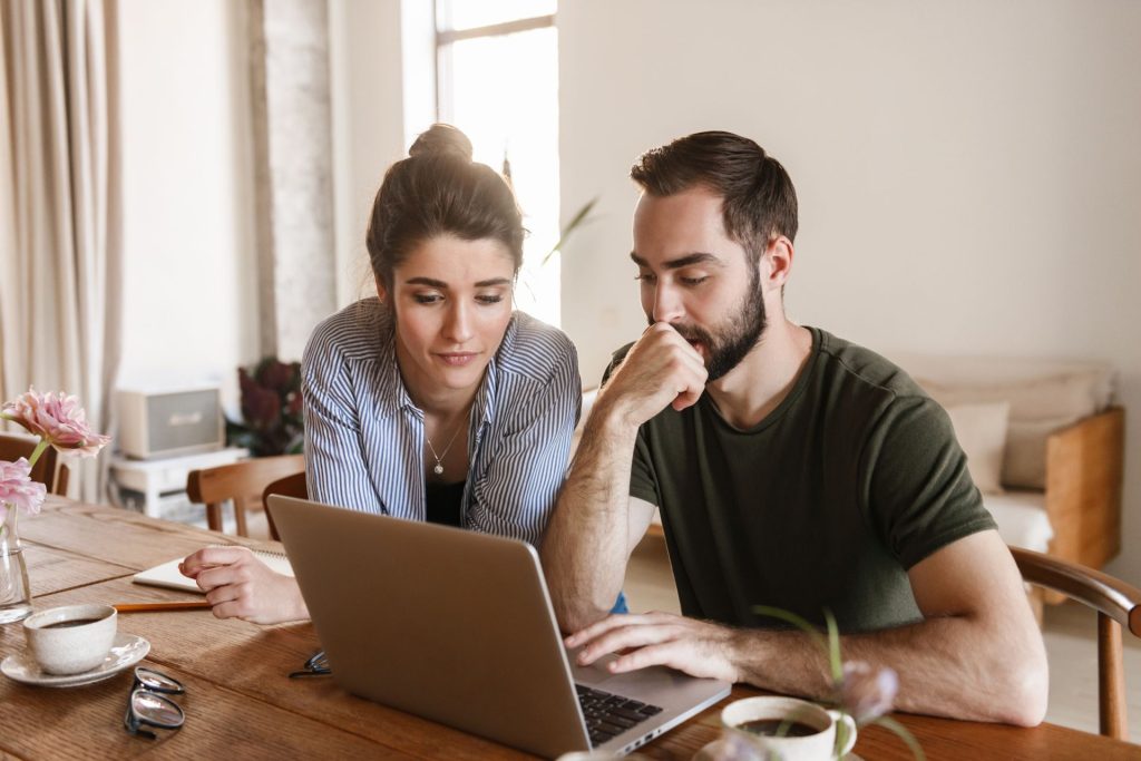 A couple seated at a table, reviewing information on a laptop as they complete their prenuptial agreement online, with a calm and collaborative atmosphere.