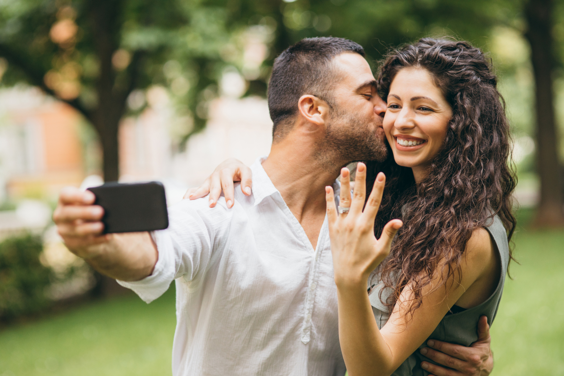 A couple taking a selfie while the man kisses the woman on the cheek, holding the phone to capture the photo.