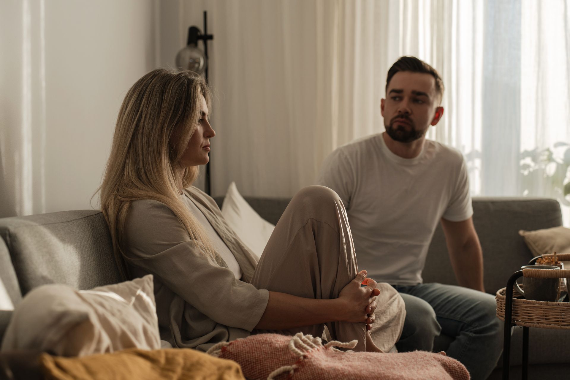 A couple sitting on a couch, turned away from each other with tense expressions, appearing to be in the middle of a disagreement