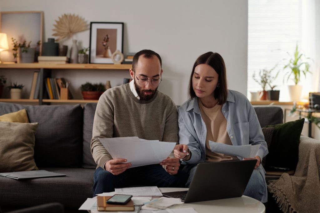 A couple sitting together at home, focused on reviewing and discussing legal documents, likely their will or estate planning paperwork.