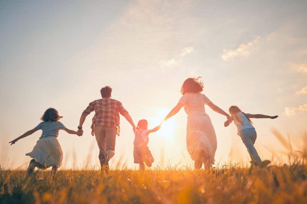 Mother, father, and three daughters running hand-in-hand at sunset, symbolizing a happy family secured and protected by a trust or will.