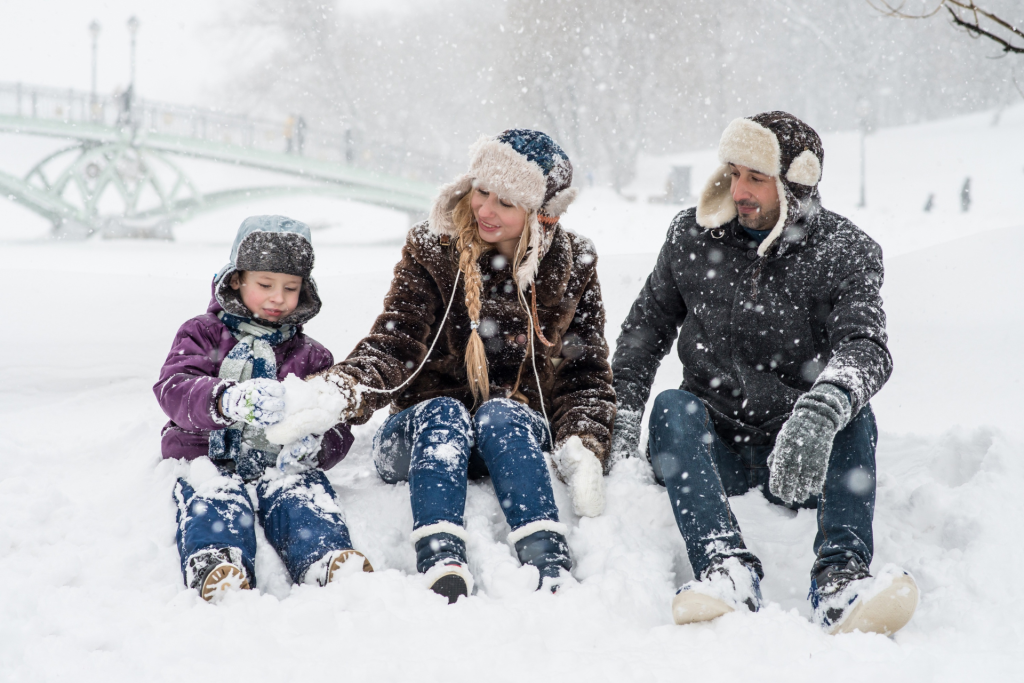 Joyful mother, father, and son bundled up and laughing while playing together in the snow during winter.
