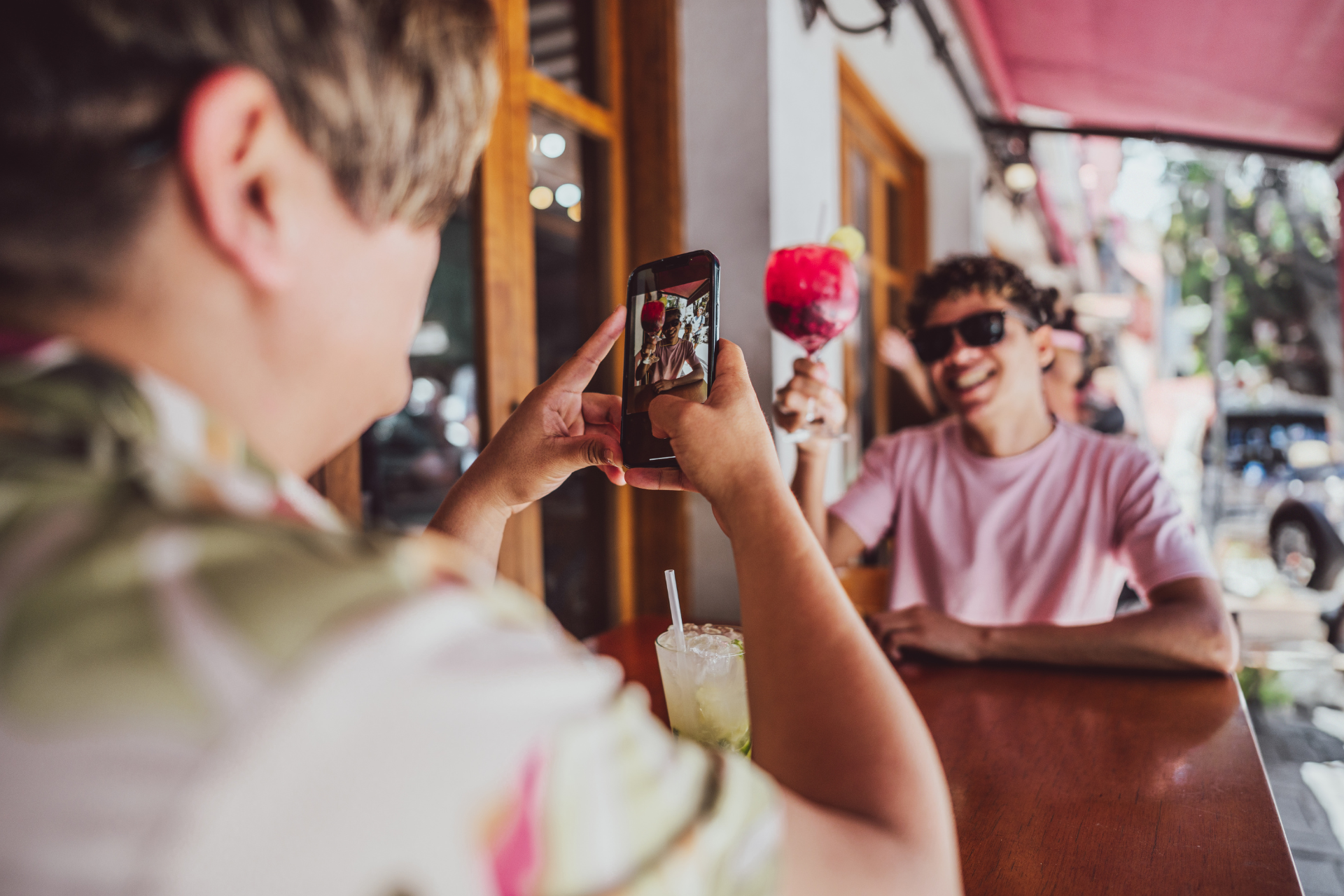 One man taking a picture of another man who is smiling and holding a wine glass during a social gathering.