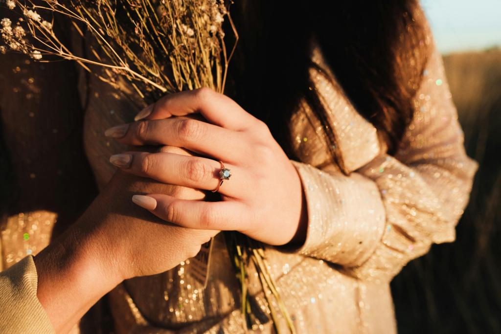 Close-up of a woman's hand holding a bouquet of flowers next to her partner's hand, clearly displaying a wedding band.