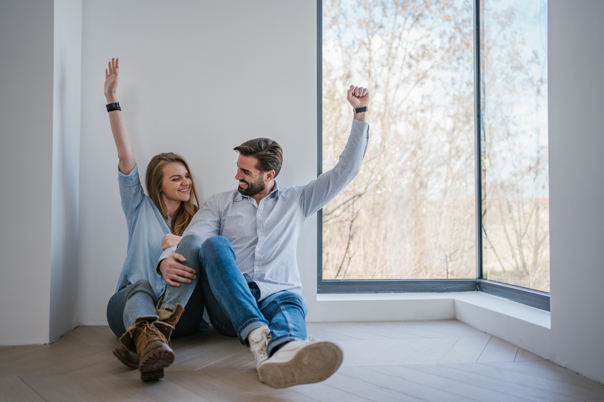 A happy couple sitting on the floor of an empty house, celebrating together as if enjoying their new home