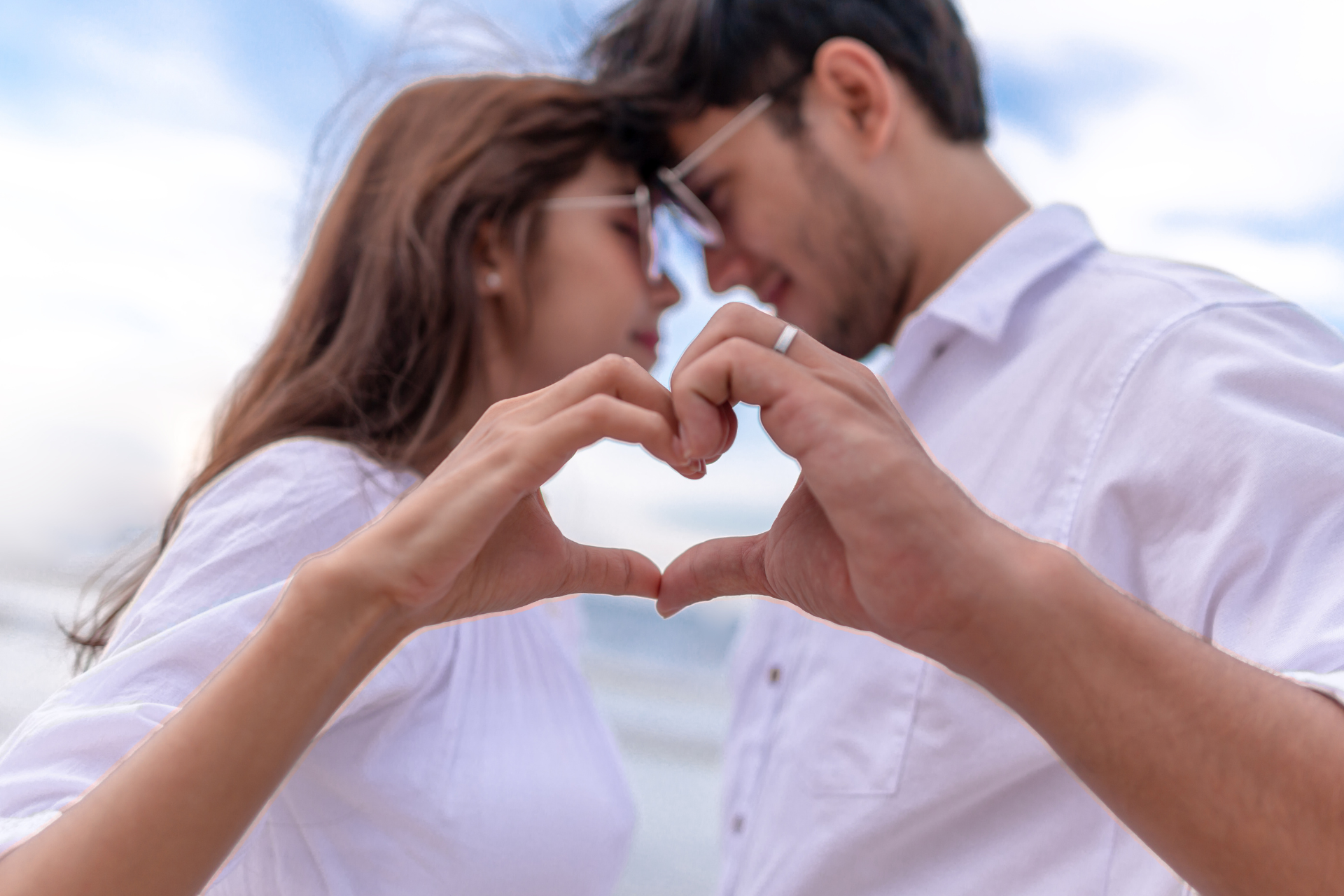 A couple looking into each other’s eyes while forming a heart shape with their hands