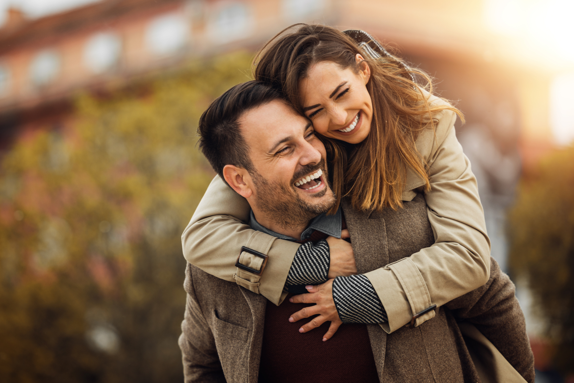 Couple Laughing and Playing Together Outdoors on an Autumn Day A couple playing outdoors on a fall day, with the woman hugging the man as he lifts her, both laughing together