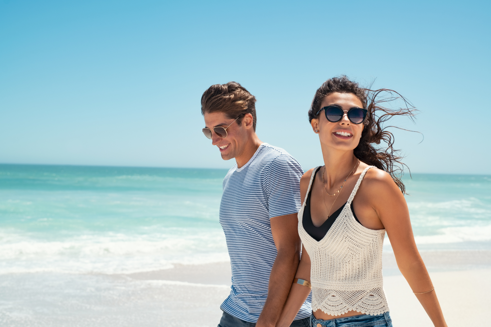 A couple walking hand in hand along the beach on a sunny day