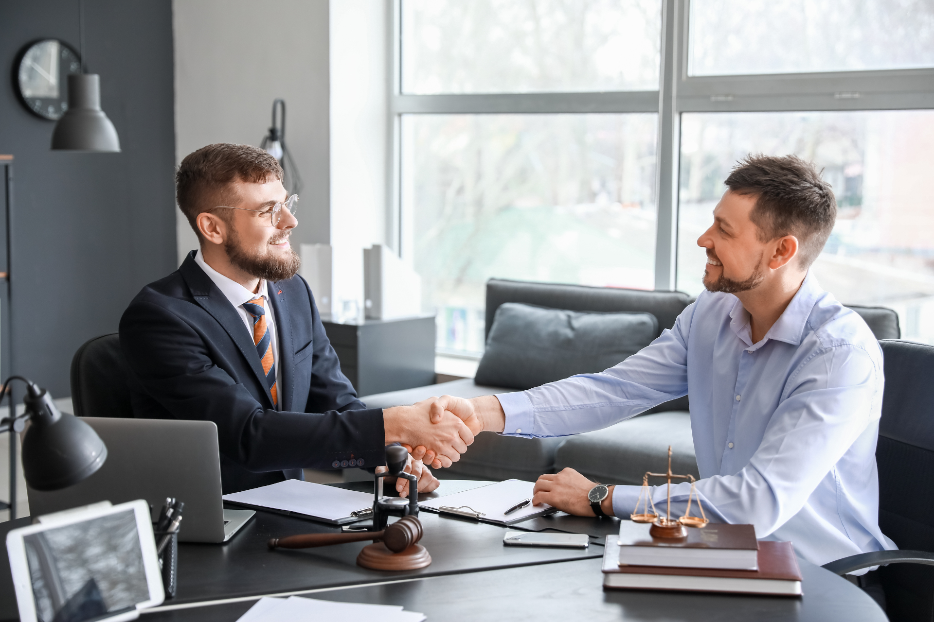 A man shaking hands with his attorney in an office setting, both smiling as if concluding a successful agreement