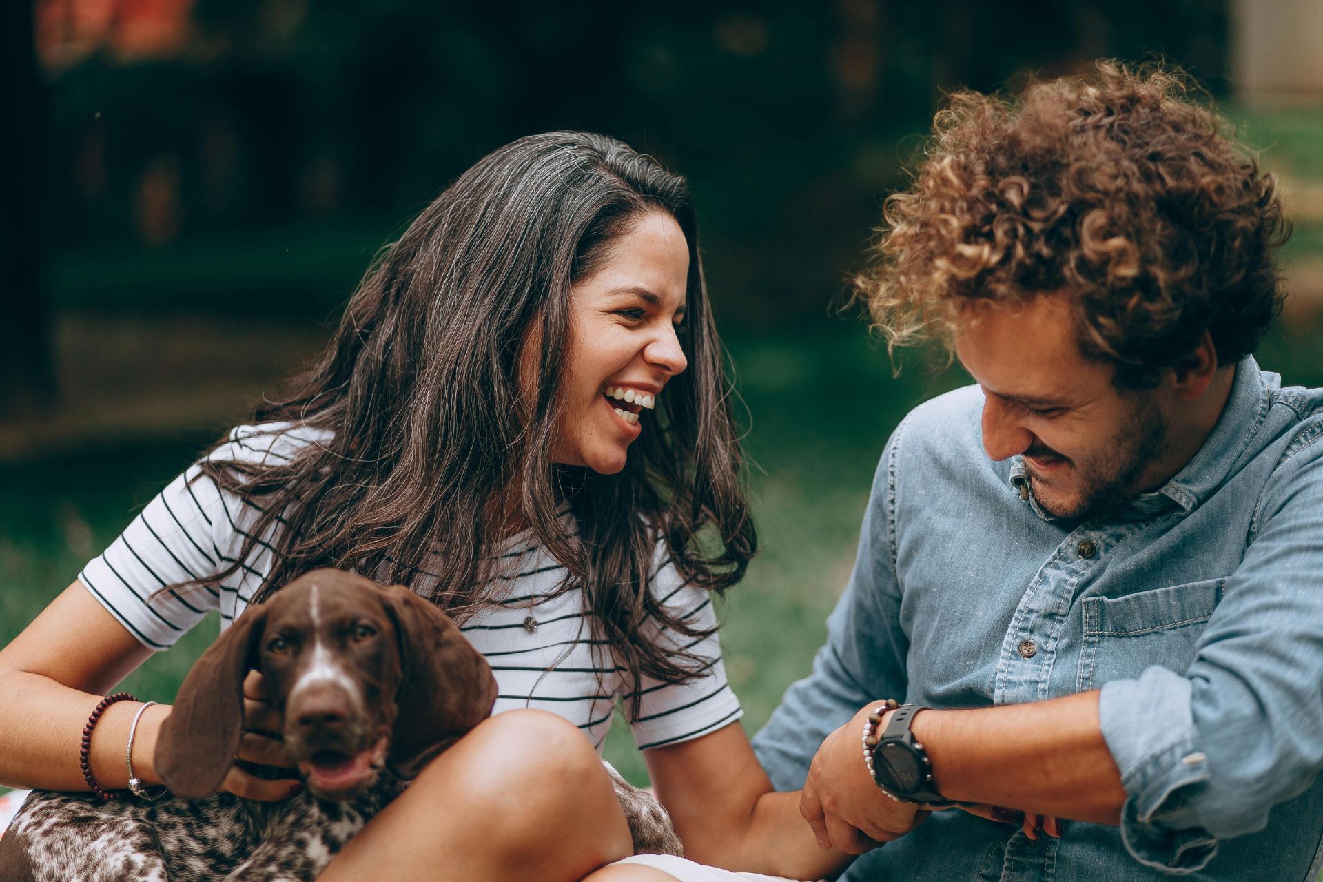 A relaxed couple laughing out loud while holding hands, as the woman holds a dog