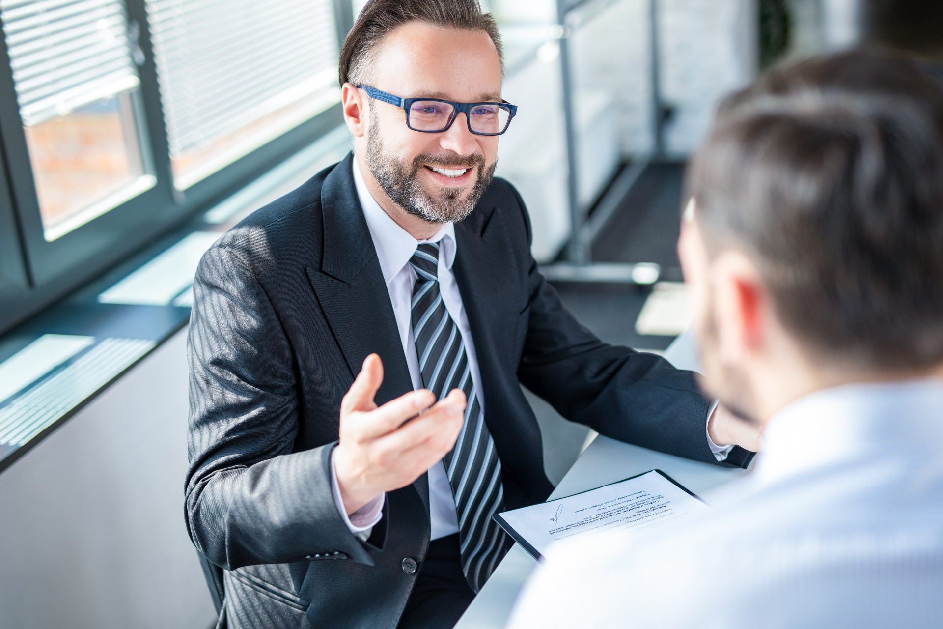 A lawyer smiling in their office while speaking with a client who is seen from behind and slightly out of focus