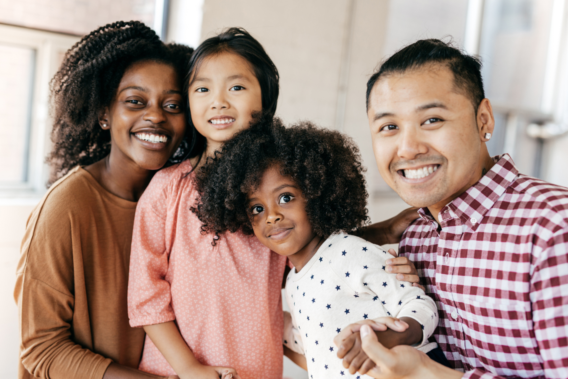 Blended family smiling together at home Two young girls with their parents smiling at the camera in a blended family setting inside their home