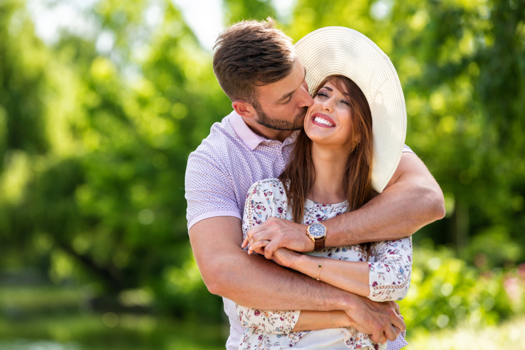 A couple hugging in a park on a sunny day, surrounded by greenery and natural light