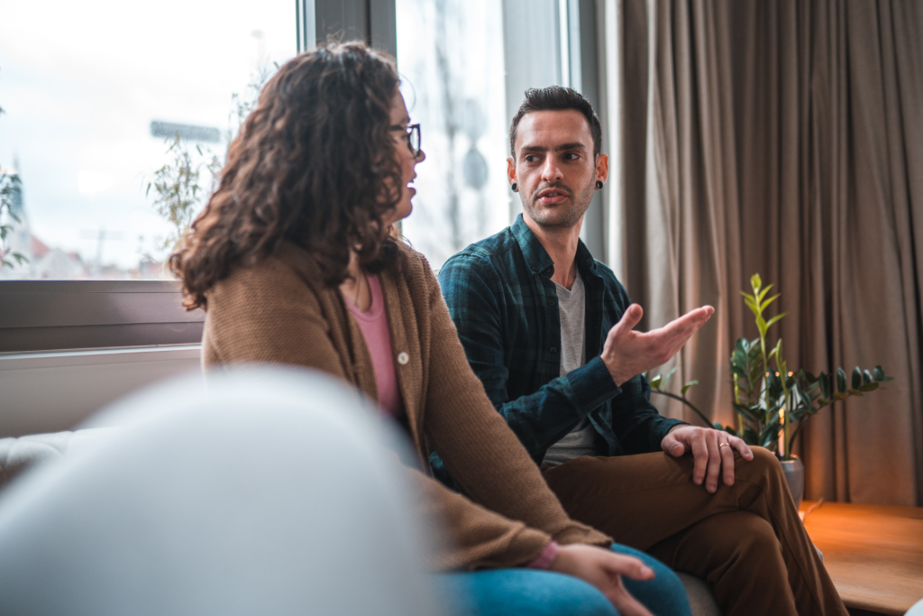 A couple sitting on a sofa engaged in a serious discussion, appearing thoughtful and calm but not smiling, as they talk about something important