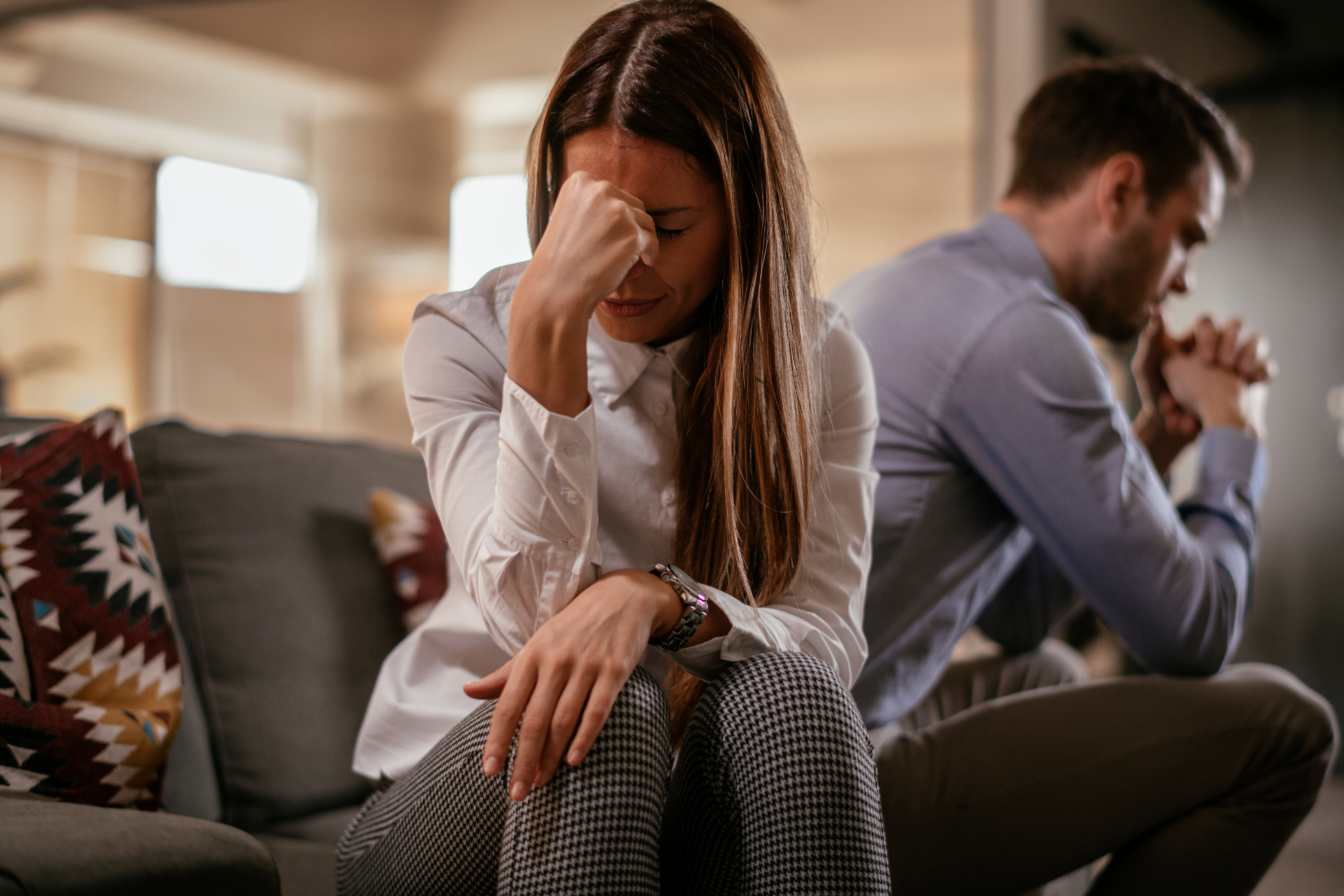 Couple sitting apart after an argument A couple sitting separately on a sofa with distance between them, both holding their heads and appearing exhausted after a disagreement