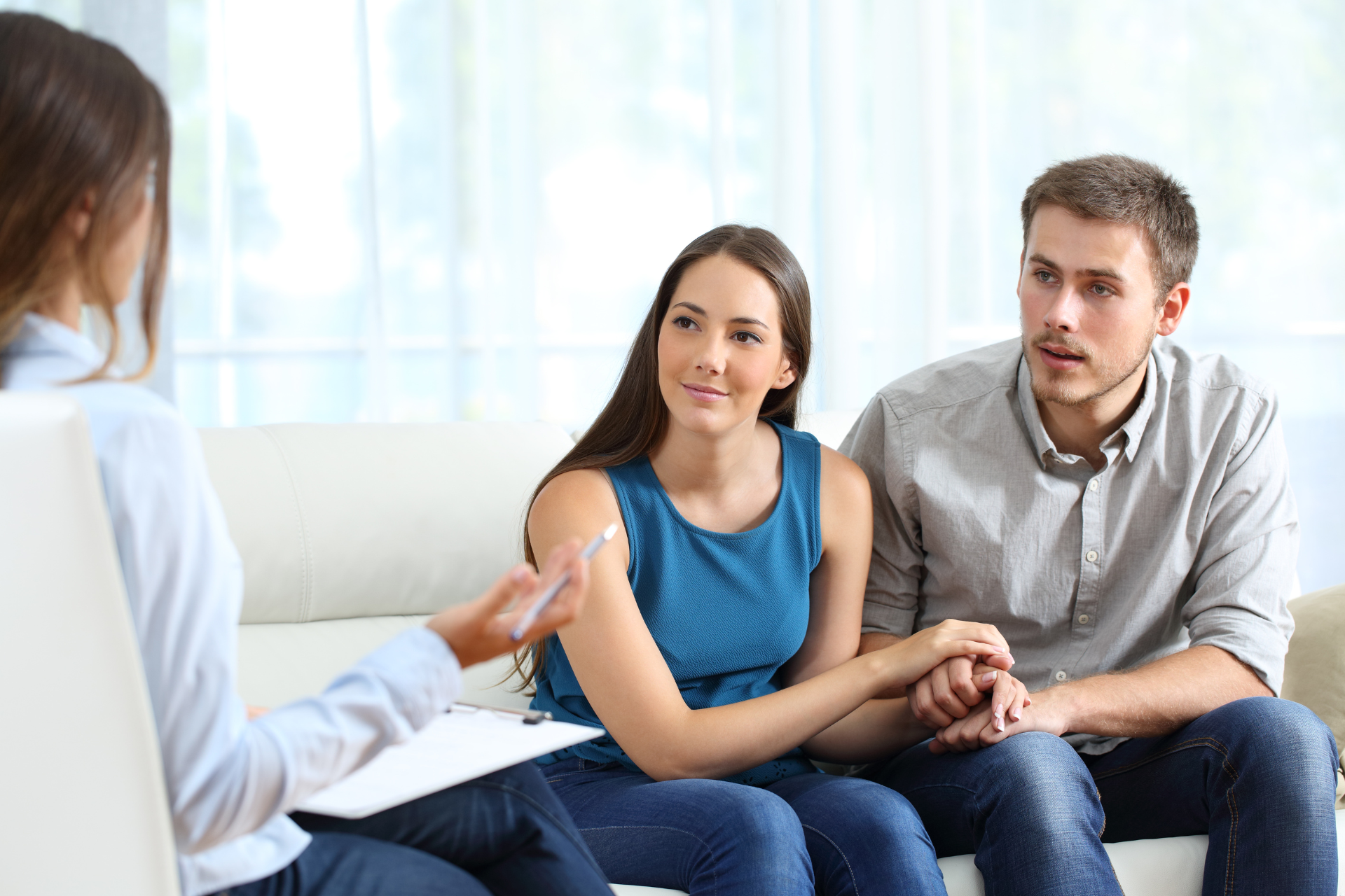 A couple sitting on a sofa talking with a therapist during a counseling session, engaged in a thoughtful and serious conversation